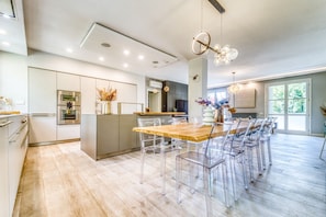 A modern kitchen with a central island, stainless steel appliances, and a dining area with clear chairs and a wooden table. - Casa Quarrata - Luxurious 120-square-meter Designer Apartment in Quarrata (Quarrata)