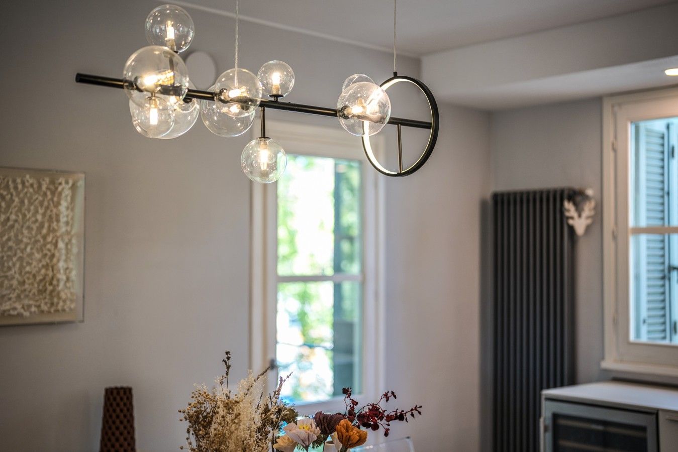 Un interior moderno con una lámpara esférica única, una ventana con persianas y un elemento decorativo en la pared.