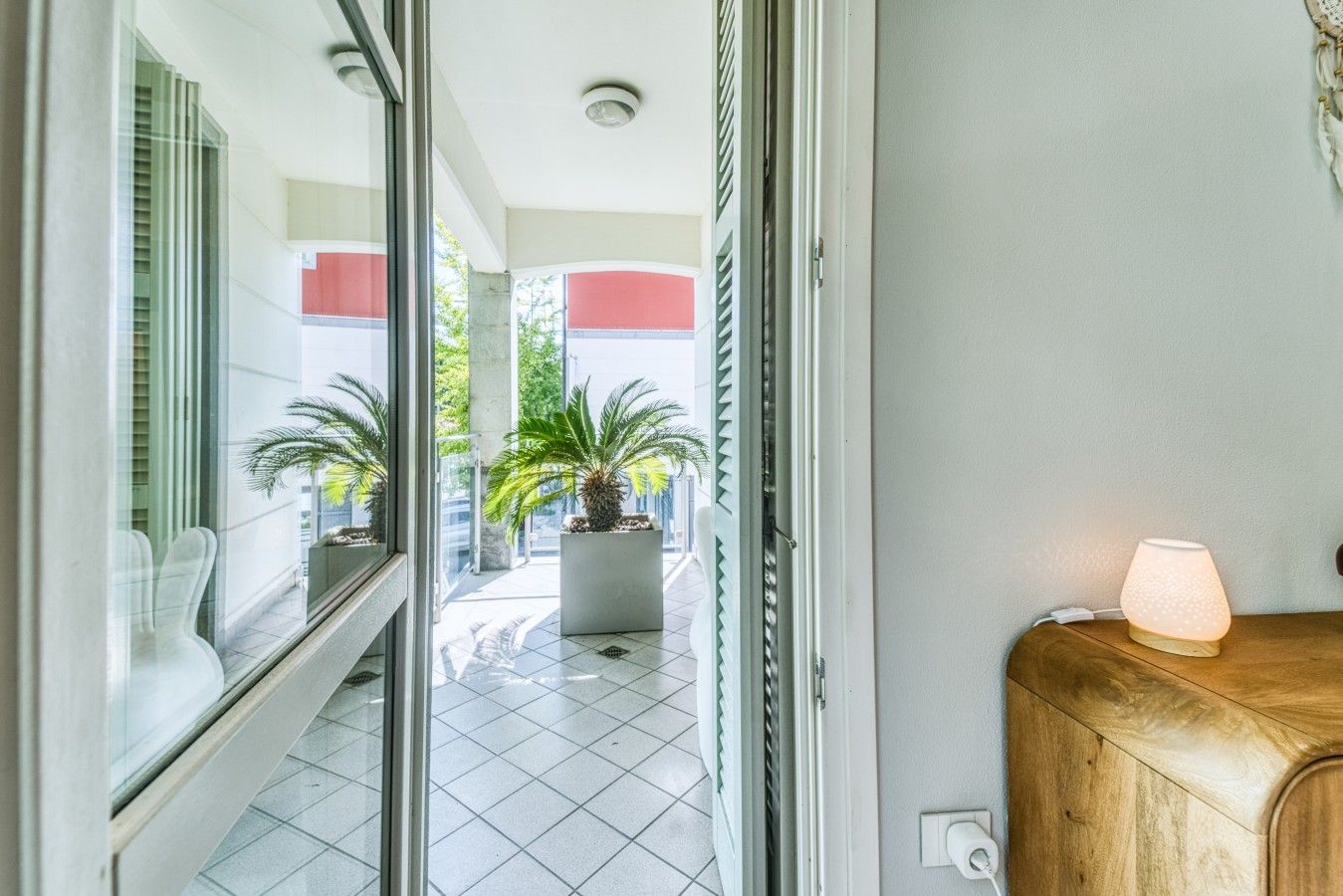 Entrada de hotel con puerta de cristal, una planta en maceta y un mostrador de madera con una lámpara.