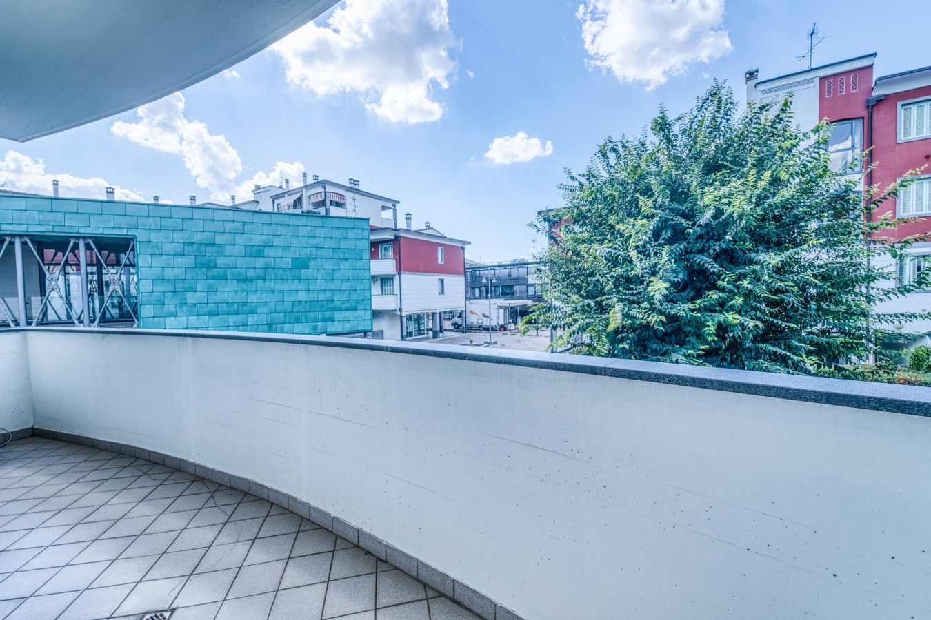 Un balcon avec un sol carrelé, une vue sur des immeubles et un arbre.