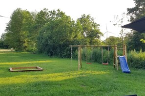 A grassy outdoor area with a wooden swing set and a slide. - Holiday home Moorweg (Treia)