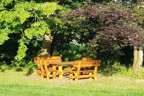 A wooden bench and picnic table in a grassy area with trees. - Holiday home Moorweg (Treia)