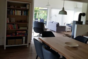 A dining area with a wooden table, chairs, a bookshelf, and a view of the outdoors. - Holiday home Moorweg (Treia)