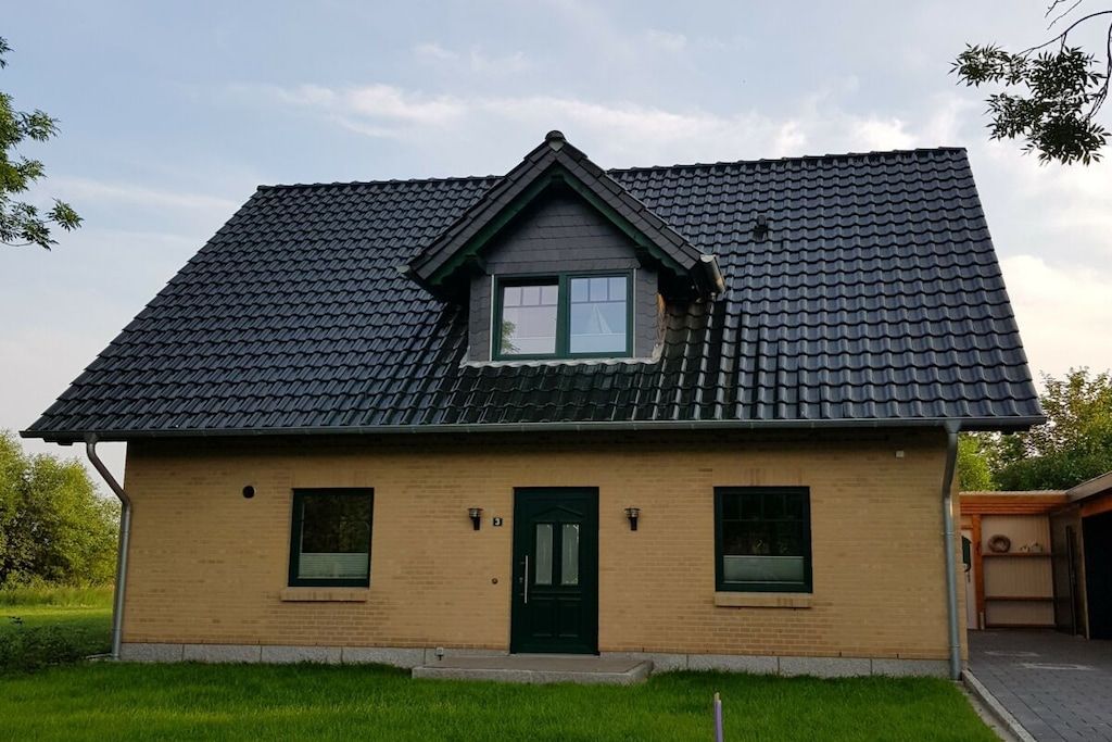 A single-story house with a dark tiled roof, a green door, and two windows on the front facade.