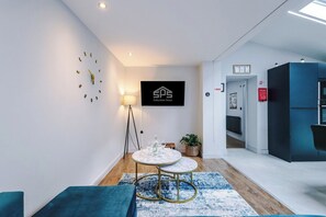 Una habitación de hotel moderna con una mesa redonda, un reloj, un logo enmarcado en la pared y una pared de acento azul.