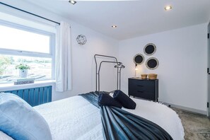 Un dormitorio con cama, radiador, ventana con cortinas, mesita de noche con cestas y decoración en la pared.