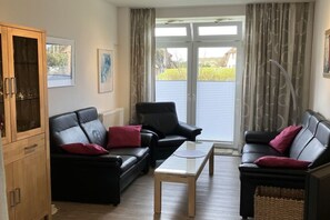 A living room with a black leather sofa, a wooden cabinet, and a glass coffee table. - Holiday apartment with 1 bedroom (List \/ Sylt)