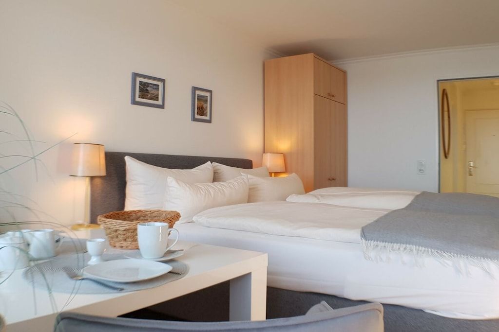 A hotel room with a bed, bedside lamps, a small table with a basket, and two framed pictures on the wall.