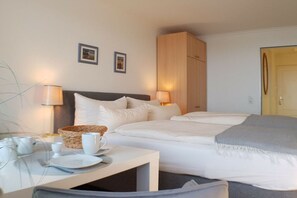 Ein Hotelzimmer mit Bett, Nachttischlampen, einem kleinen Tisch mit einem Korb und zwei gerahmten Bildern an der Wand.