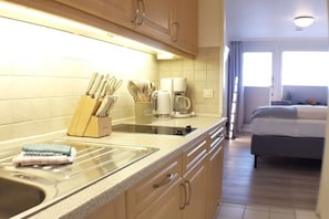 Eine Küche mit Spüle, Arbeitsplatte und Schränken. Im Hintergrund ist ein Bett zu sehen.