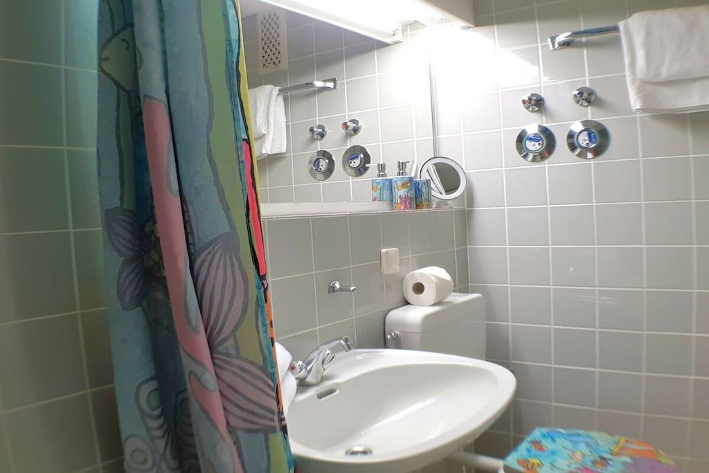 Un baño con lavamanos blanco, un espejo y una ducha con cortina.