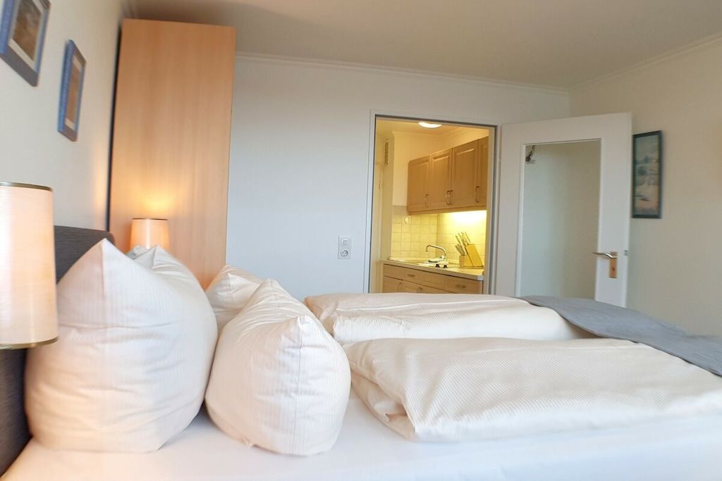 Une chambre d’hôtel comprenant un lit, des oreillers, une lampe de chevet, une porte donnant sur une salle de bain et une vue sur une cuisine.