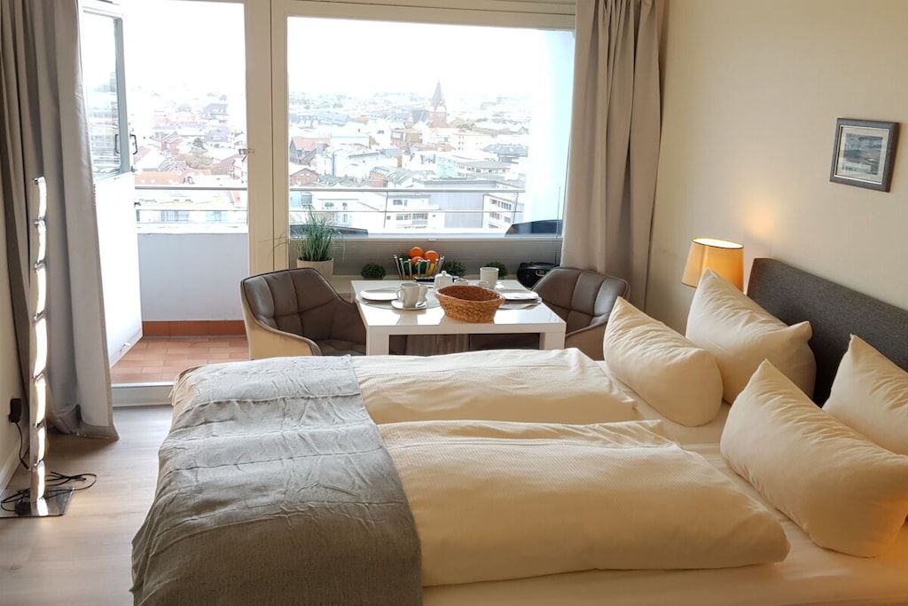 Ett hotellrum med en säng, ett matbord med stolar, utsikt över staden och en lampa på nattduksbordet.