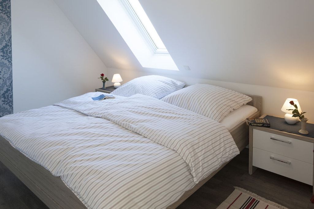 A bedroom with a sloped ceiling, a bed with striped bedding, a bedside table with a lamp, and a small plant.
