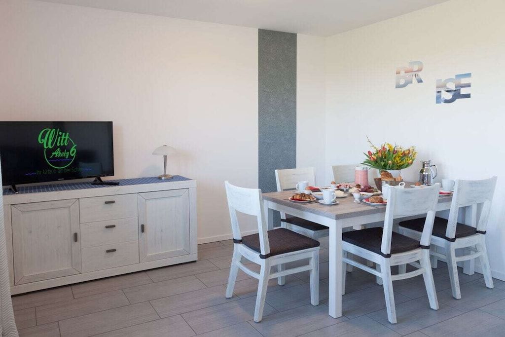Ein Essbereich mit einem weißen Tisch, vier Stühlen und einem Fernseher auf einem Schrank.