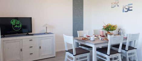 A dining area with a white table, four chairs, and a television on a cabinet.