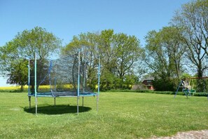 Ein Trampolin in einer grünen Umgebung mit Bäumen und einer Schaukel im Hintergrund.