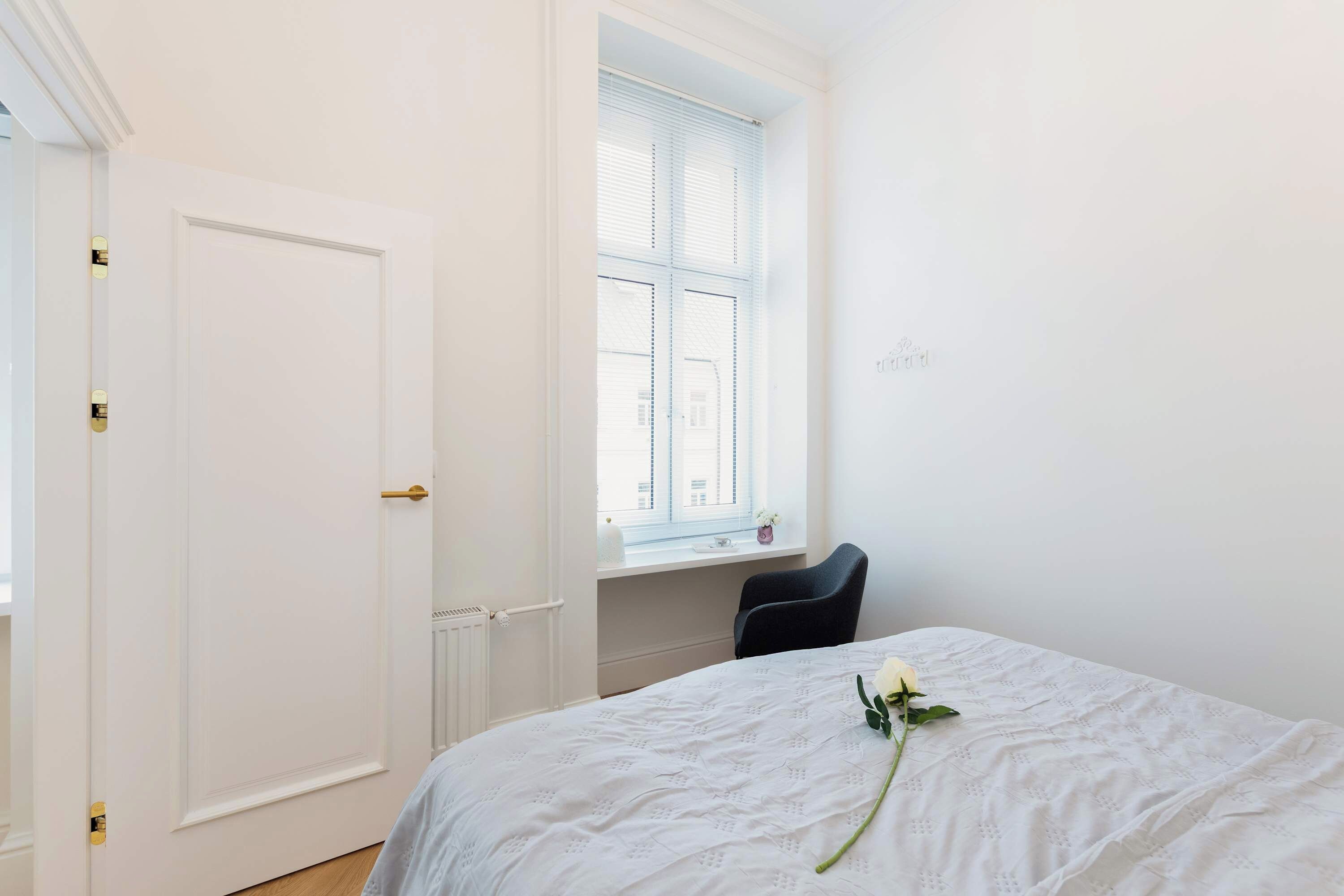 Ein Zimmer mit einem Bett, einem Fenster mit Jalousien, einem Heizkörper und einer Tür.
