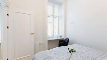 Ein Zimmer mit einem Bett, einem Fenster mit Jalousien, einem Heizkörper und einer Tür.