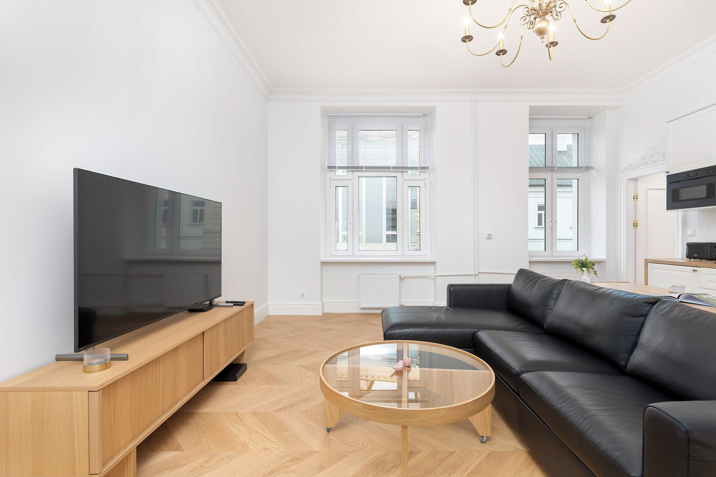 Una sala de estar moderna con un televisor de pantalla plana, un sofá de cuero, una mesa de centro de vidrio y una araña.