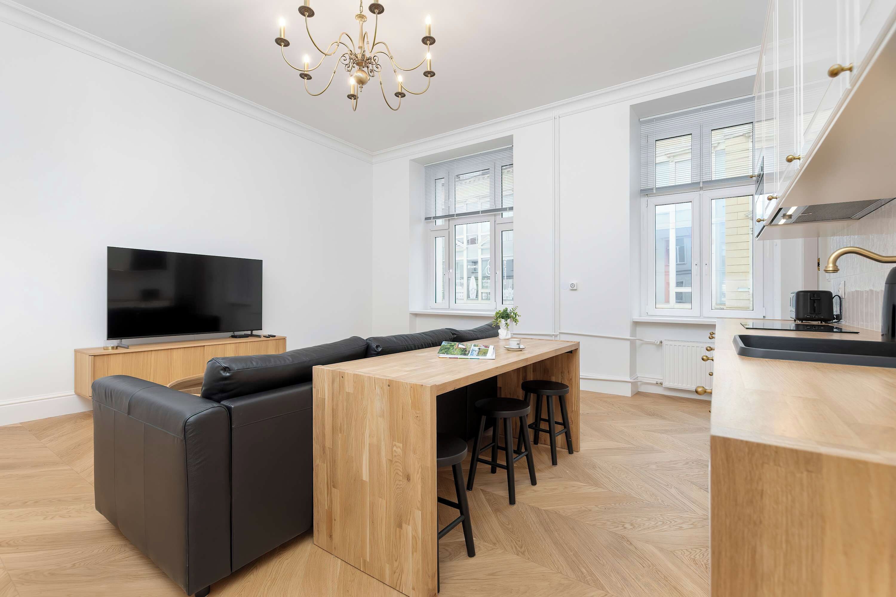A modern kitchen with a built-in TV, wooden dining table, and black bar stools.