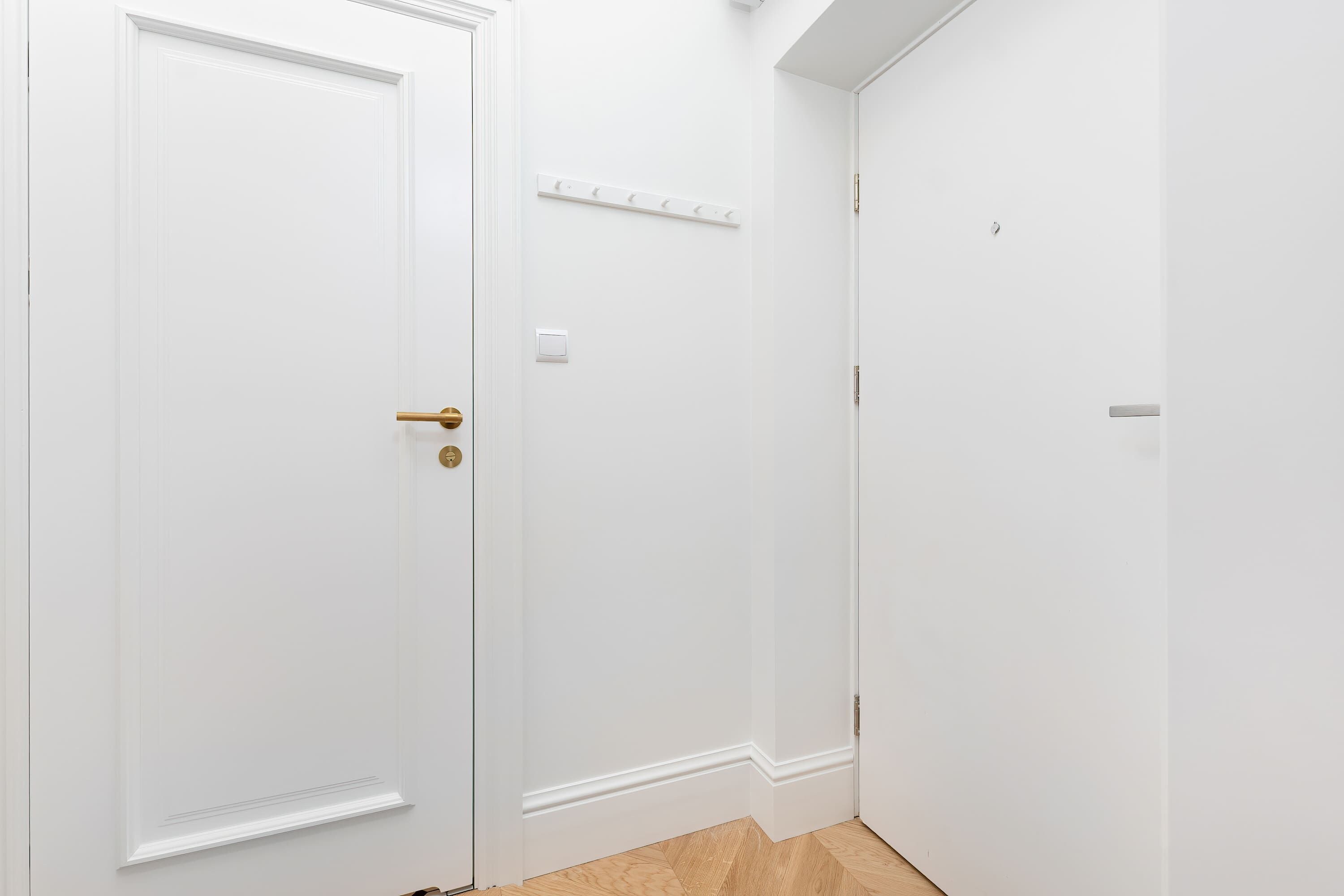 Un pasillo con dos puertas blancas, una con picaporte de latón y un interruptor de luz encima.