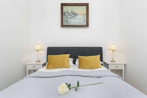Ein ordentlich bezogenes Bett mit zwei Kissen, einer einzelnen Rose und einem Gemälde darüber.
