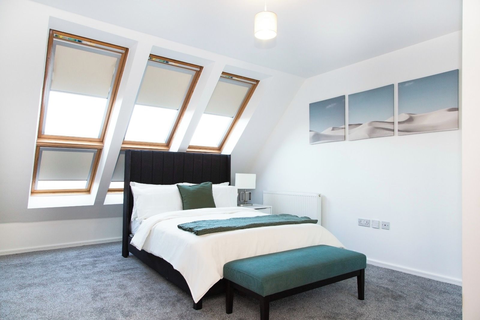 Ein Schlafzimmer mit einem Bett, einer Bank, Dachfenstern, einer Heizung und Kunstwerken an der Wand.