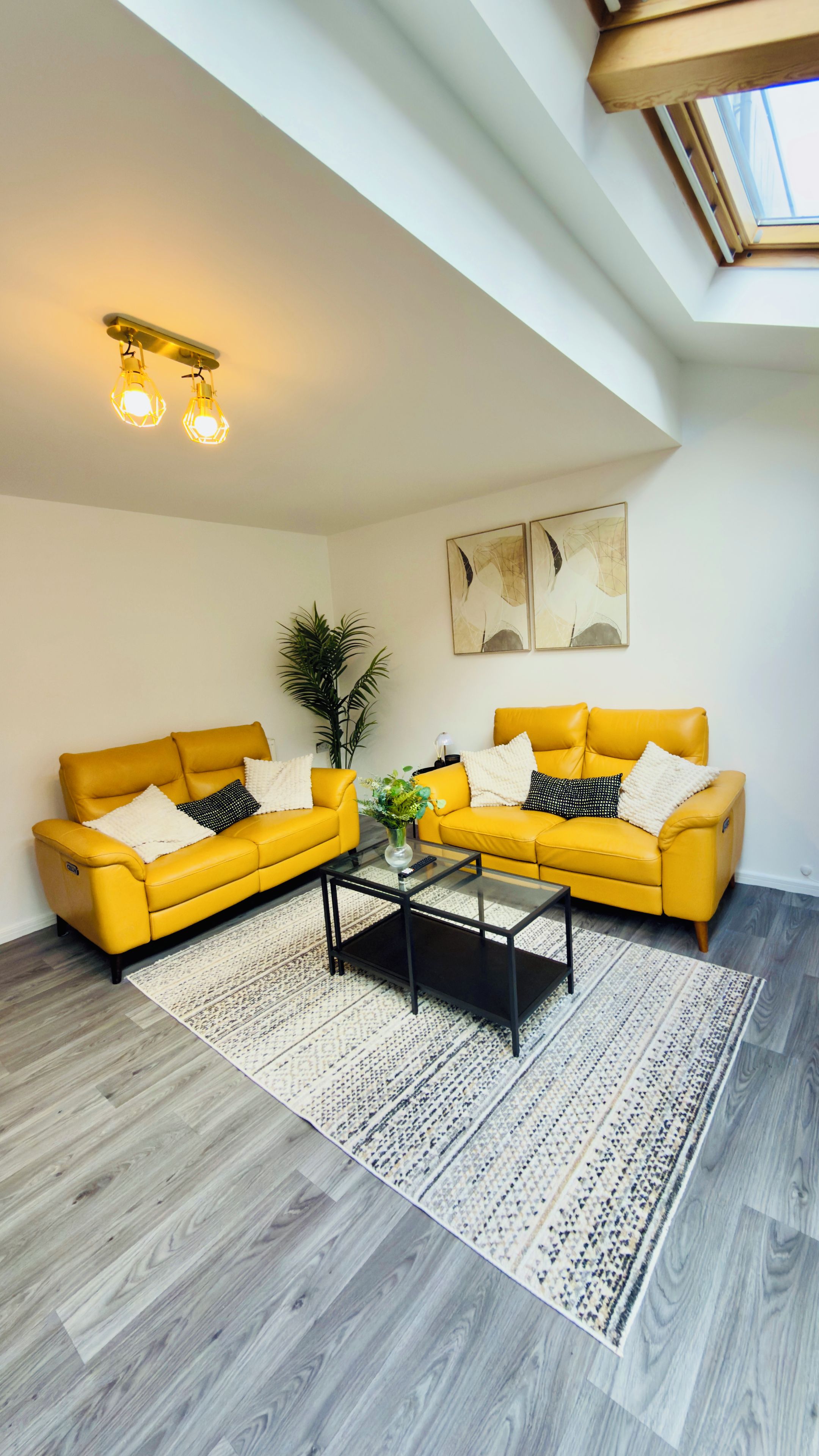 Ein modernes Wohnzimmer mit zwei gelben Sofas, einem Glastisch und einem großen Fenster.