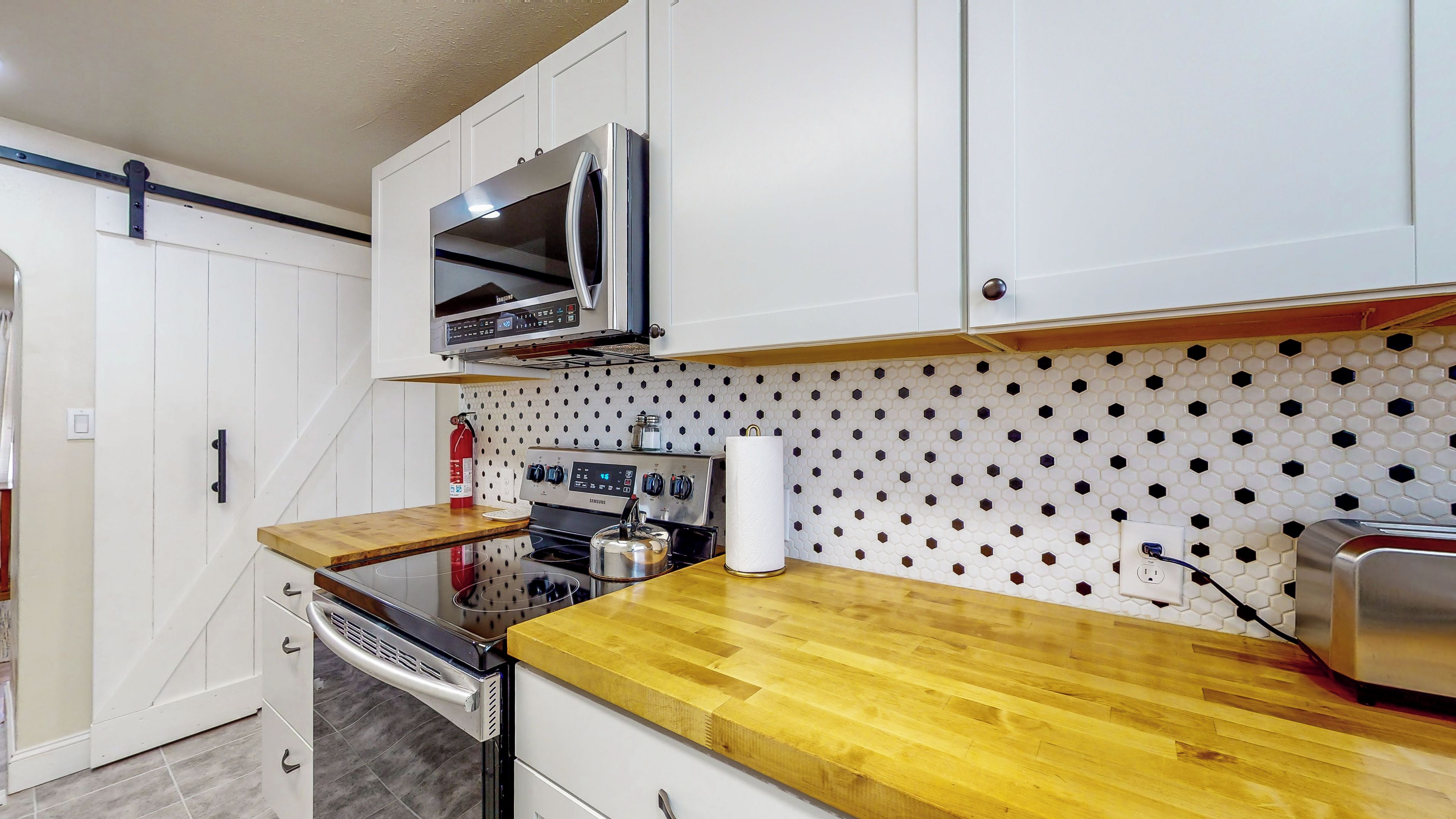 A compact kitchen with white cabinets, a stainless steel oven, a microwave, and a wooden countertop.