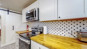 A compact kitchen with white cabinets, a stainless steel oven, a microwave, and a wooden countertop.
