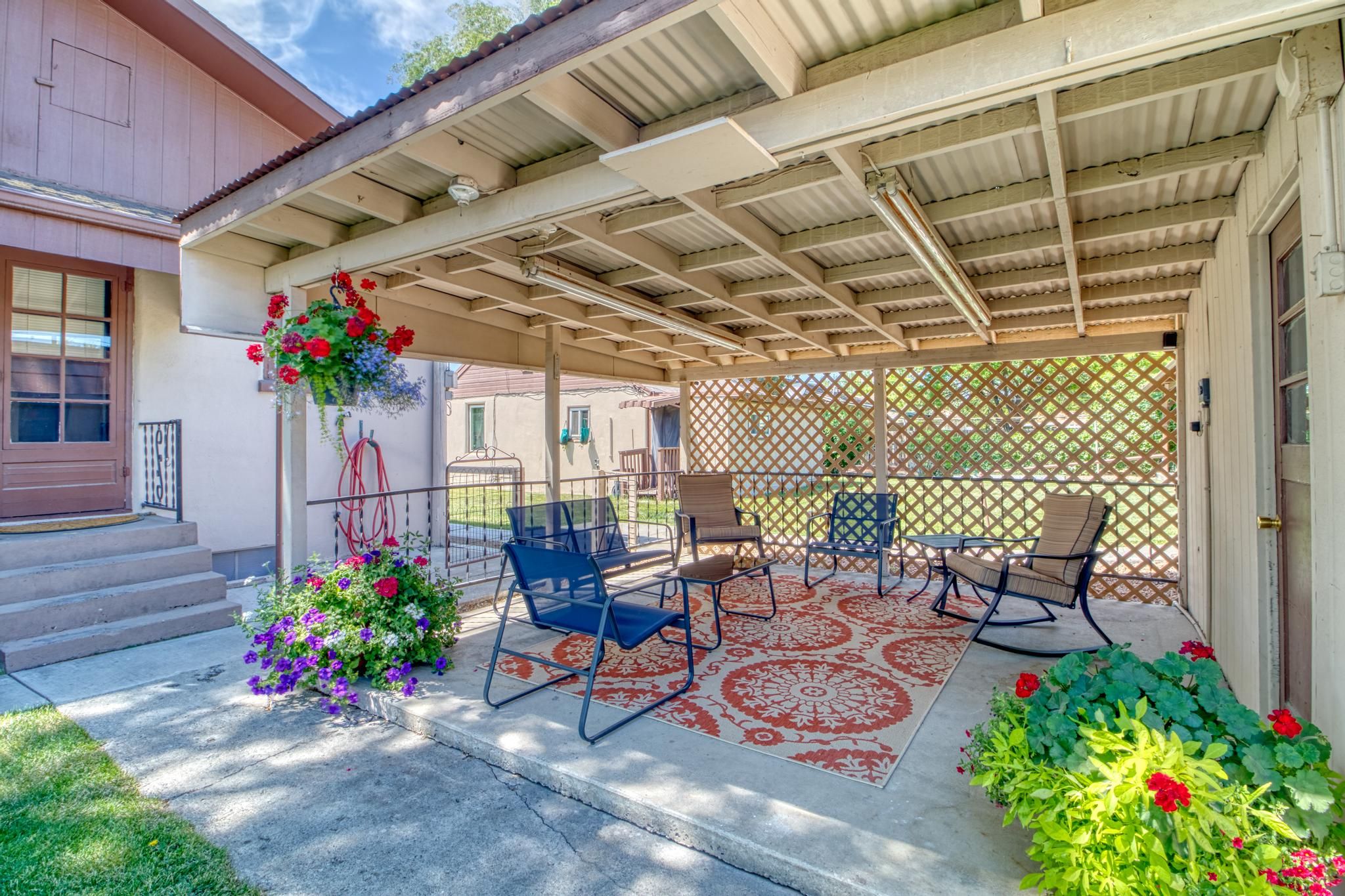 A covered patio with outdoor furniture, a decorative flower arrangement, and a lattice fence.