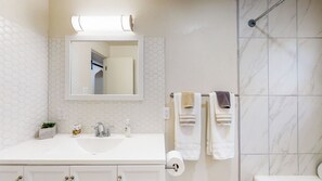 Un baño con un lavabo blanco, un espejo, un perchero con toallas y una zona de ducha.