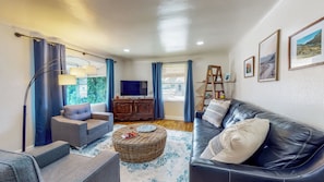 A living room with a sofa, armchair, TV, wooden cabinet, and a bookshelf.