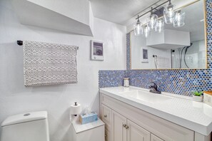 Une salle de bain avec un lavabo blanc, un miroir orné d’une mosaïque bleue et une serviette accrochée au mur.