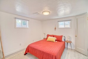 Une chambre à coucher avec un grand lit, deux fenêtres, une porte et un luminaire au plafond.