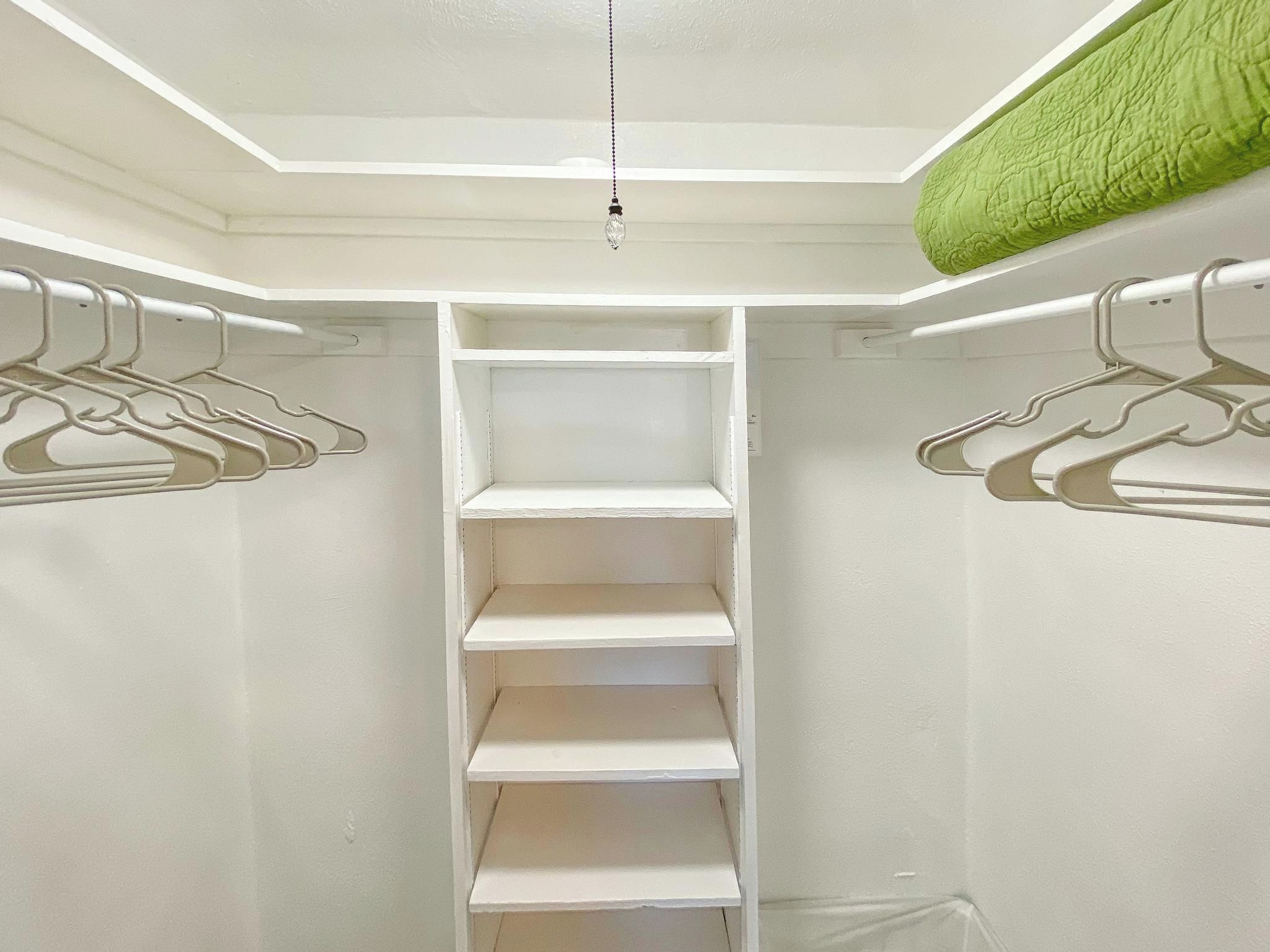 Ein begehbarer Kleiderschrank mit weißen Wänden, einer Hängeleuchte und einem grünen Stoffelement an der Decke.