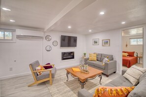 Un salon moderne avec un canapé gris, une chaise en bois, une table basse et un téléviseur fixé au mur.