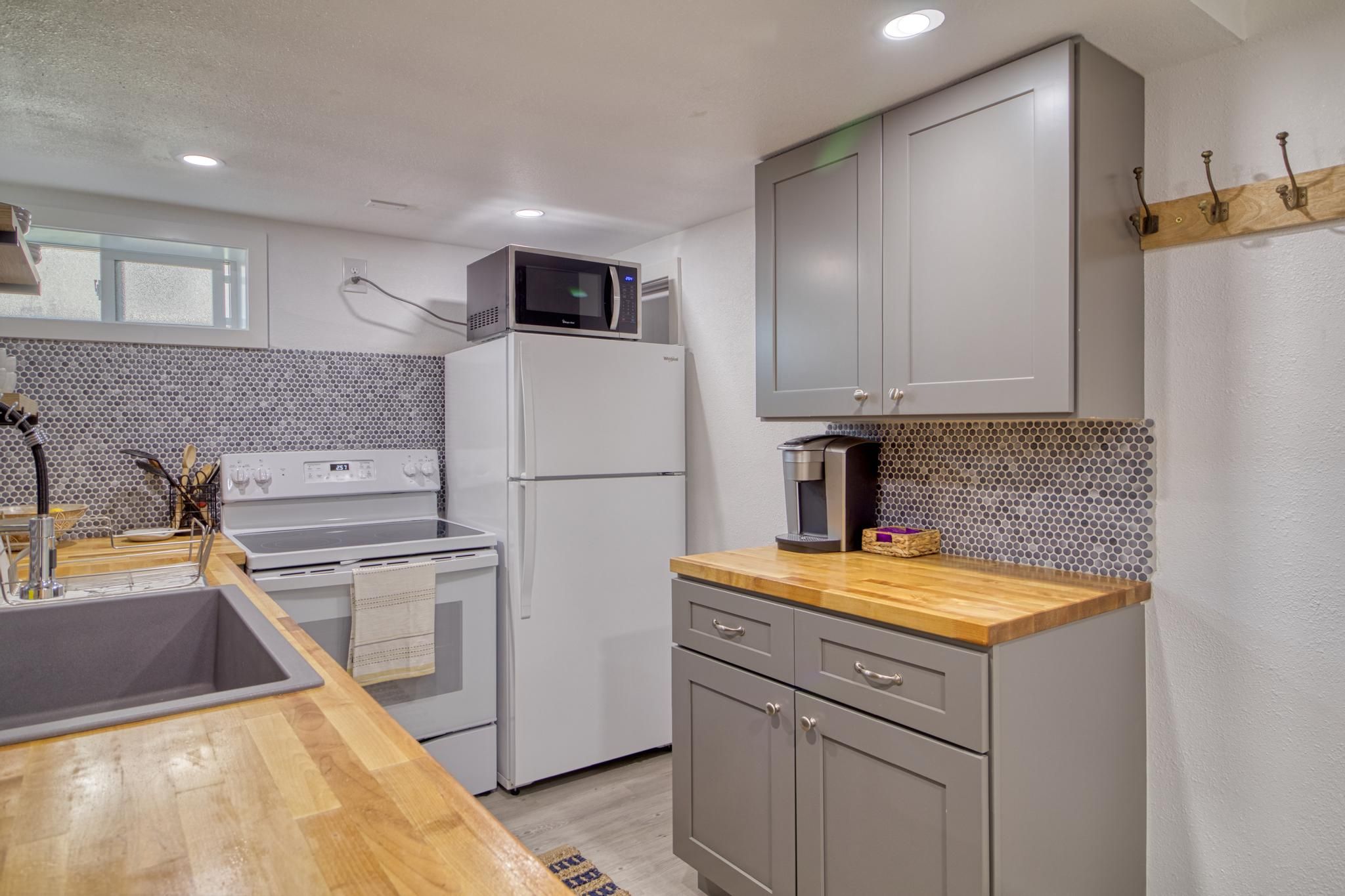 A compact kitchen with a microwave on top of a refrigerator, a coffee maker on the counter, and a sink with a wooden countertop.