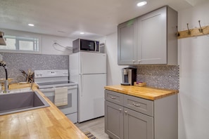 A compact kitchen with a microwave on top of a refrigerator, a coffee maker on the counter, and a sink with a wooden countertop.