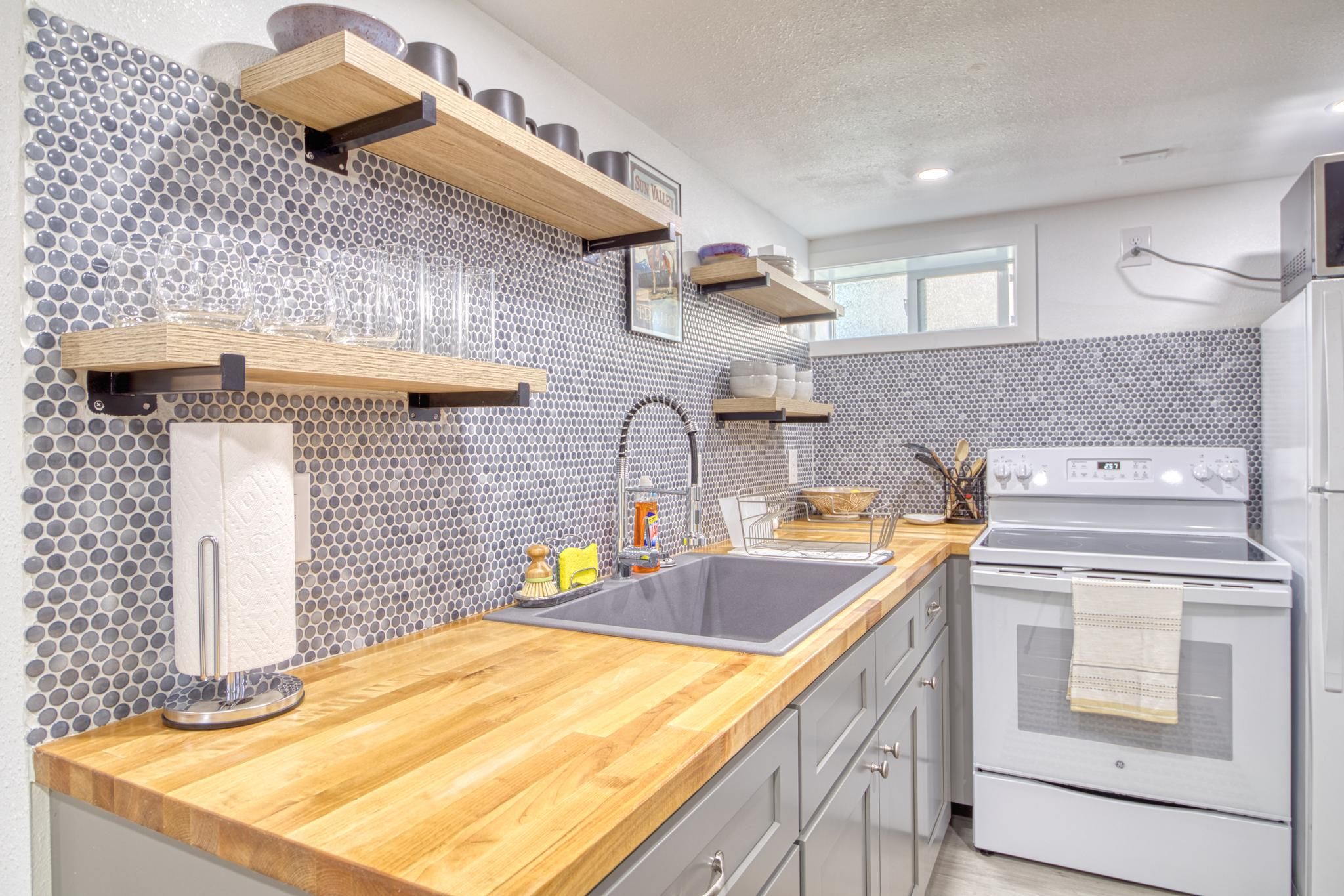 A modern kitchen with a wooden countertop, a stainless steel sink, a built-in oven, and a backsplash with hexagonal tiles.