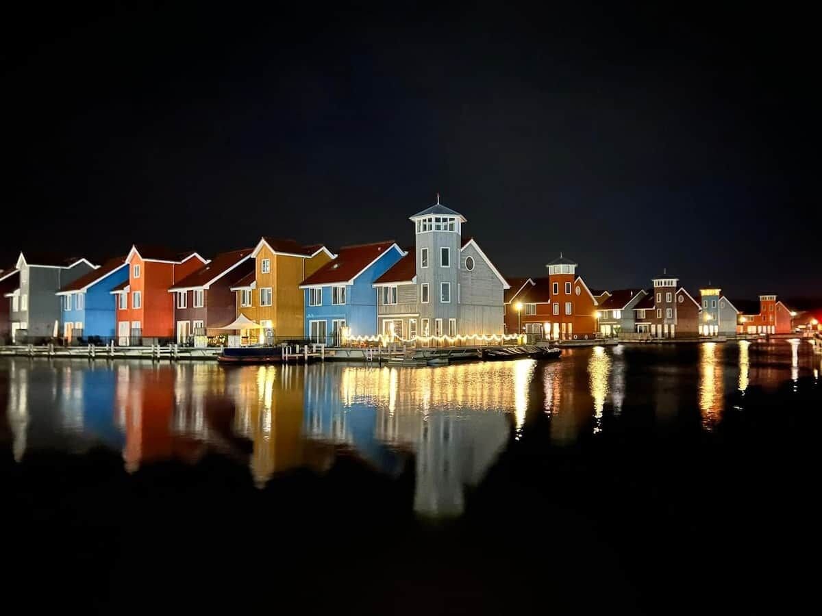 Een pand aan het water met meerdere gebouwen, een steiger en een rustig waterlichaam dat de gebouwen weerspiegelt.