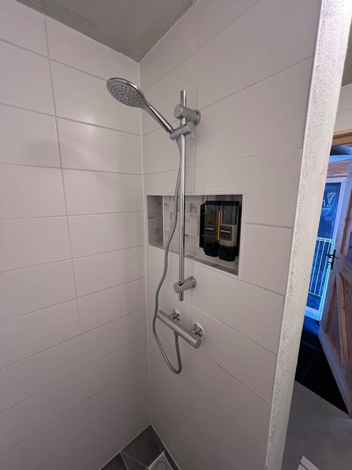 Une douche équipée d’un pommeau de douche à main et d’un robinet mural.