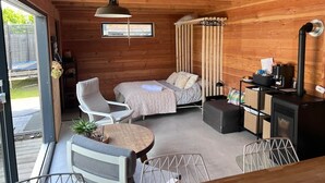 L’intérieur d’un chalet accueillant, avec un lit, deux fauteuils, une petite table et un poêle à bois.