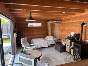 Een knus interieur van een blokhut met een bed, twee stoelen, een kleine tafel en een houtkachel.
