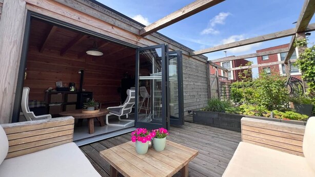 Une terrasse extérieure avec des meubles en bois, une table décorée de fleurs et une porte vitrée donnant sur un espace intérieur.