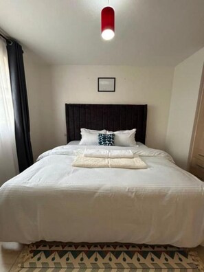 Quarto de hotel com uma cama grande, cabeceira, mesa de cabeceira e luminária vermelha.