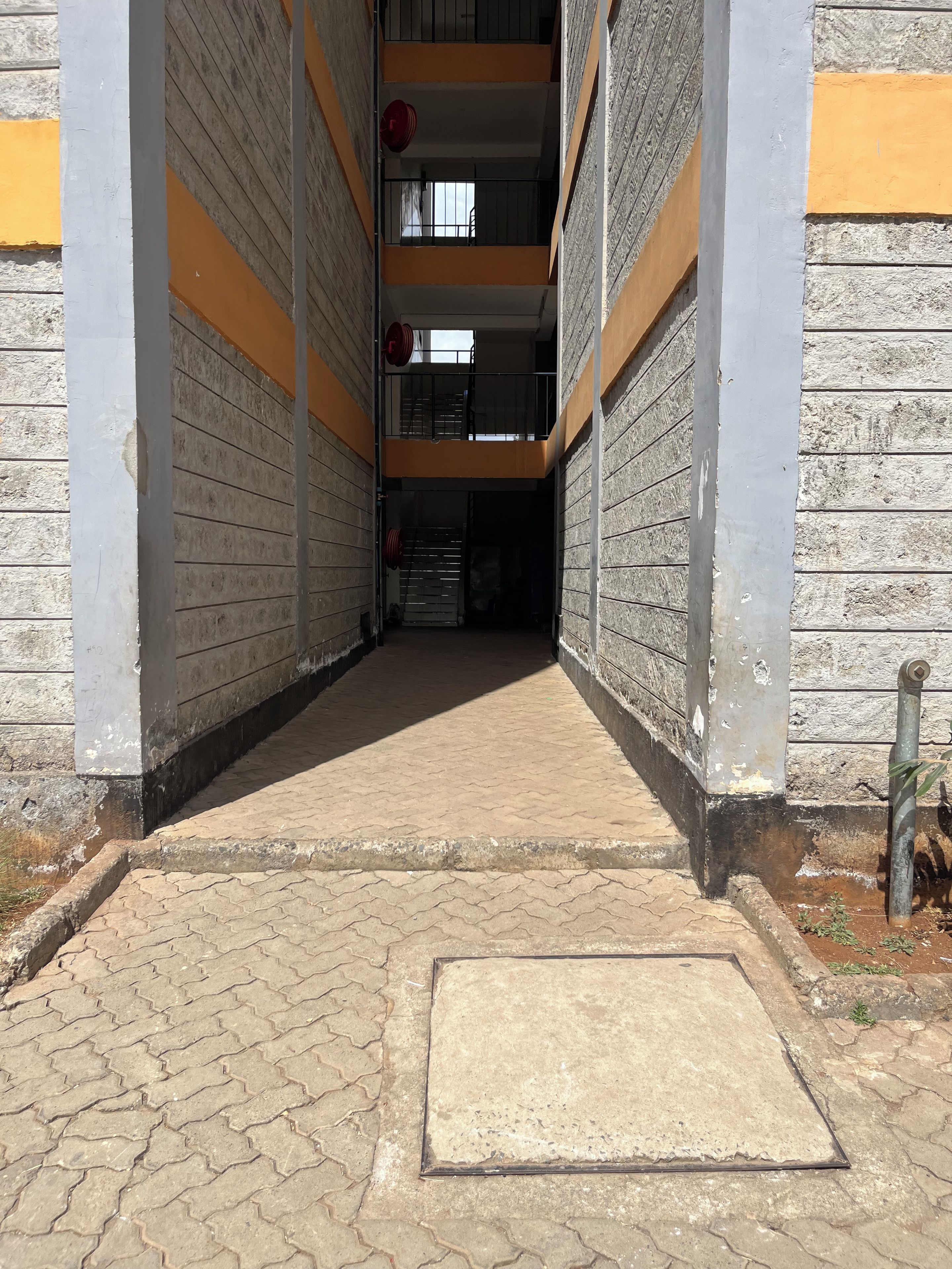 A corridor with a tiled floor leading to a door, flanked by walls with a brick pattern and yellow accents.