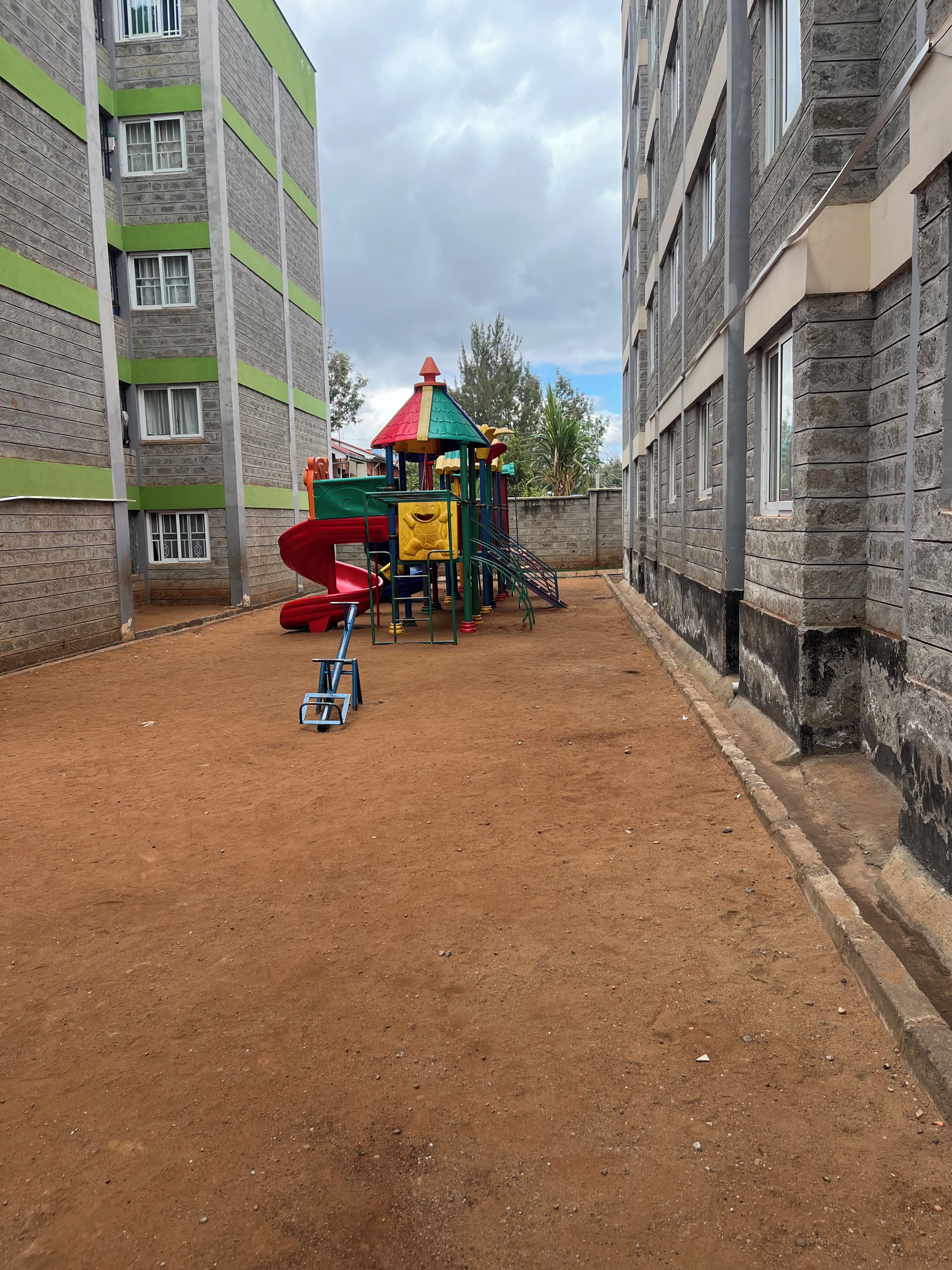 Een speeltuin met glijbanen en klimconstructies, omgeven door gebouwen met bakstenen gevels en ramen.