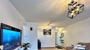 A modern living room with a flat-screen TV, a black coffee table, a beige sofa, and a unique geometric pendant light. - Serene 2-bedroom apartment in wonderful Ongata Rongai location (Ongata Rongai)